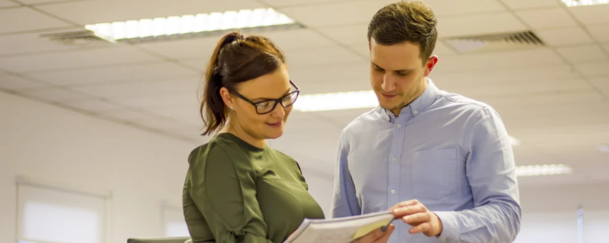 Two young professionals in an office, reviewing a document together