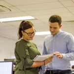 Two young professionals in an office, reviewing a document together